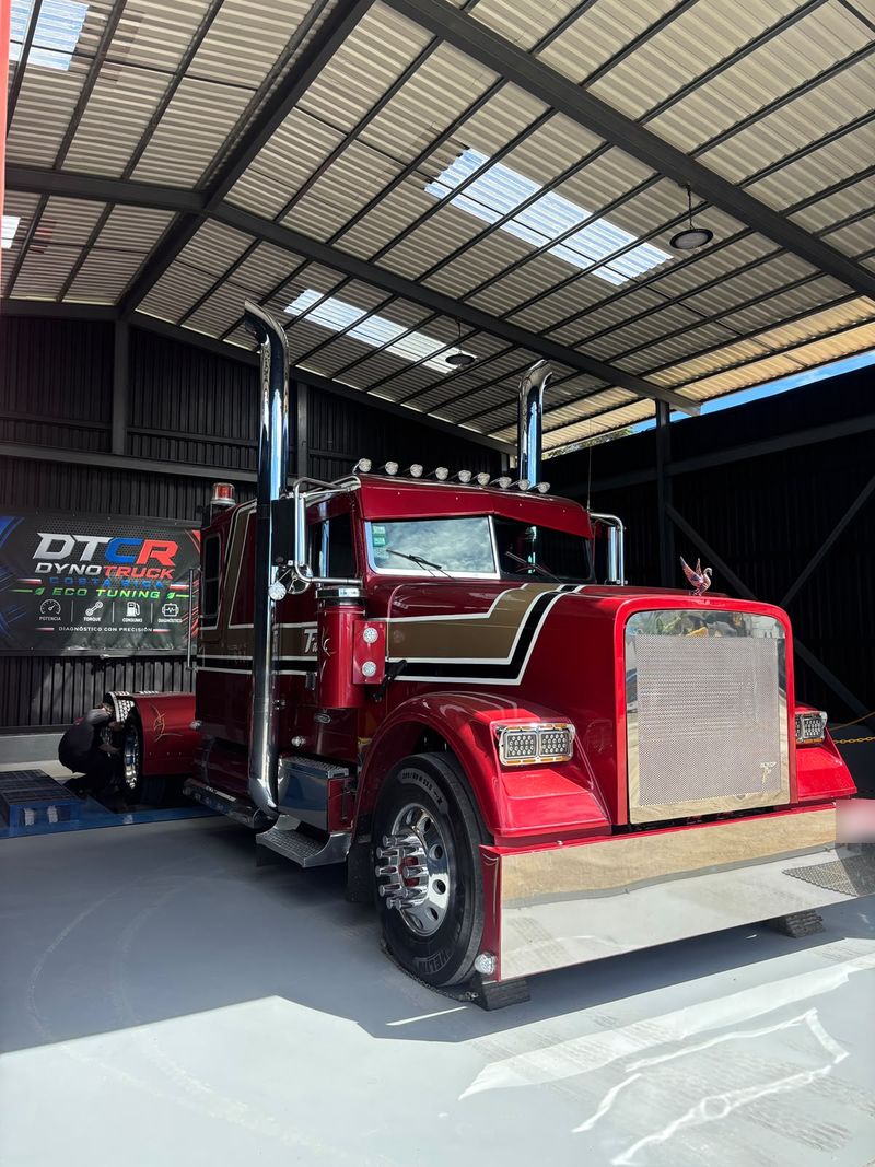 Tractocamión clásico de capó largo, rojo con franjas doradas y escapes cromados, ubicado en el dinamómetro de Dyno Truck Costa Rica frente al rótulo DTCR.