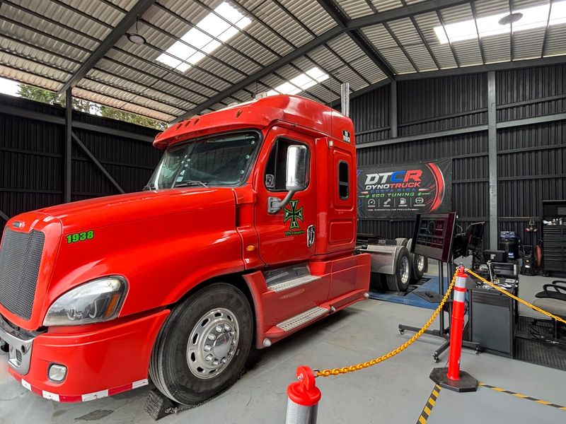Tractocamión rojo con las ruedas traseras sobre el dinamómetro, cadenas de delimitación y la estación de control con monitores a la derecha.